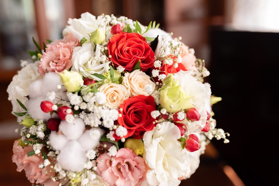 A round floral bouquet featuring a mix of red roses, cream and blush roses, white lisianthus, pink eustoma, and delicate white baby's breath, all arranged with green foliage. The flowers are fresh wit